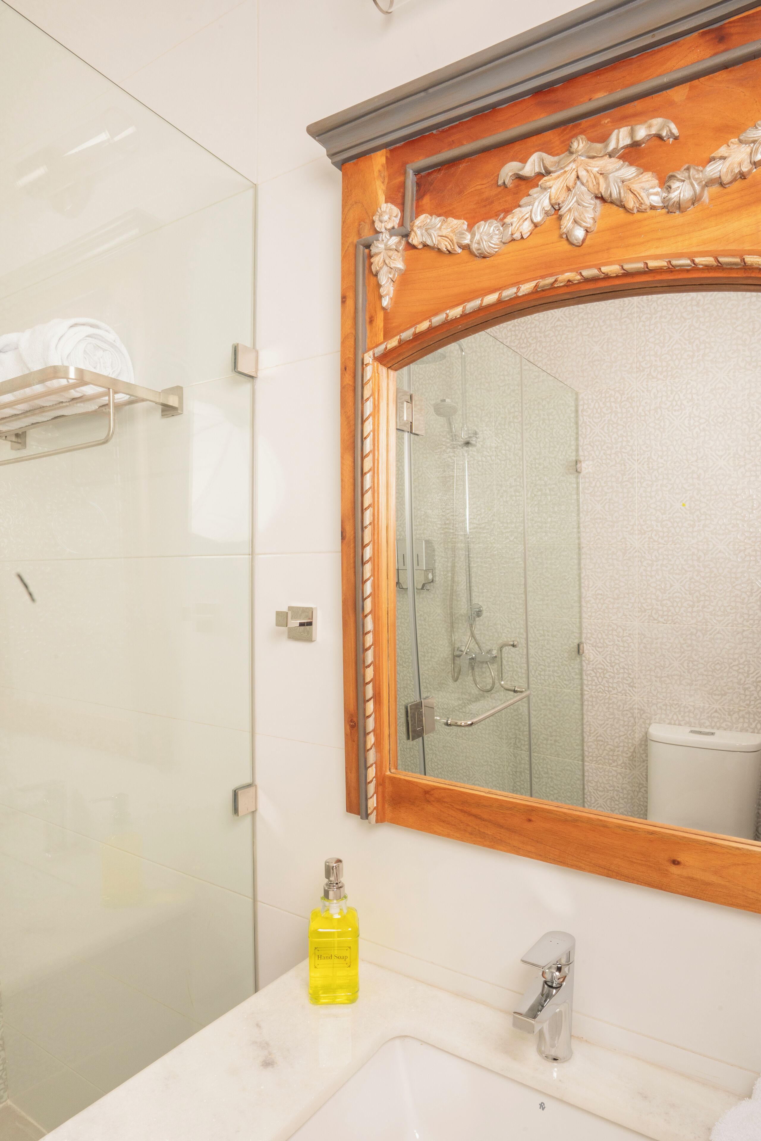 A bathroom with a glass shower enclosure, a wooden-framed mirror, and a white sink.