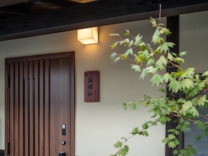 Une porte en bois ornée de panneaux verticaux, un luminaire fixé au mur et une enseigne avec des caractères japonais.