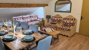 A dining area with a wooden table set for six, surrounded by chairs. A sofa with patterned cushions is against the wall, and a mirror hangs above it. - Summer/winter rental, ski - hiking Haute-Savoie - peaceful location - friends/family (La Rivière-Enverse)