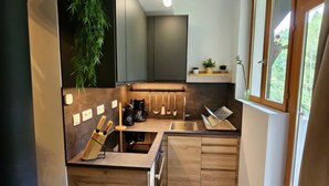 A modern kitchen with wooden cabinets, a built-in stove, and a window overlooking a garden. - Summer/winter rental, ski - hiking Haute-Savoie - peaceful location - friends/family (La Rivière-Enverse)