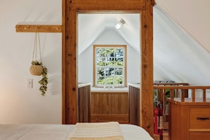 Quarto com teto de madeira, janela com vista para vegetação, planta pendente e extintor de incêndio.