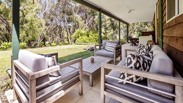 A covered outdoor seating area with wooden furniture and a view of a garden. - Ryma Cottage | Prevelly (Prevelly)