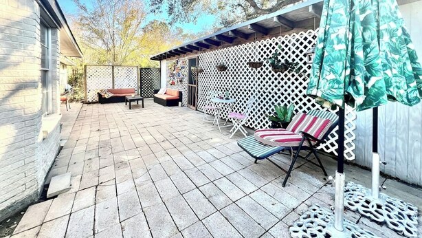 A patio with stone tiles, a white lattice fence, and outdoor furniture including a striped chair and a table. - 1960's Time Capsule, in Alvin, Tx (Alvin)