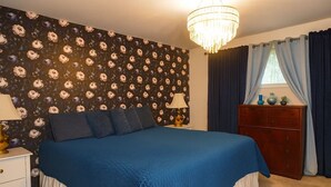 A bedroom with a large bed, a nightstand, a dresser, a chandelier, and floral wallpaper. - 1960's Time Capsule, in Alvin, Tx (Alvin)