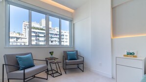 Un salon moderne doté d’une grande fenêtre, de deux canapés gris avec des coussins bleus, d’une petite table d’appoint et d’un meuble blanc.