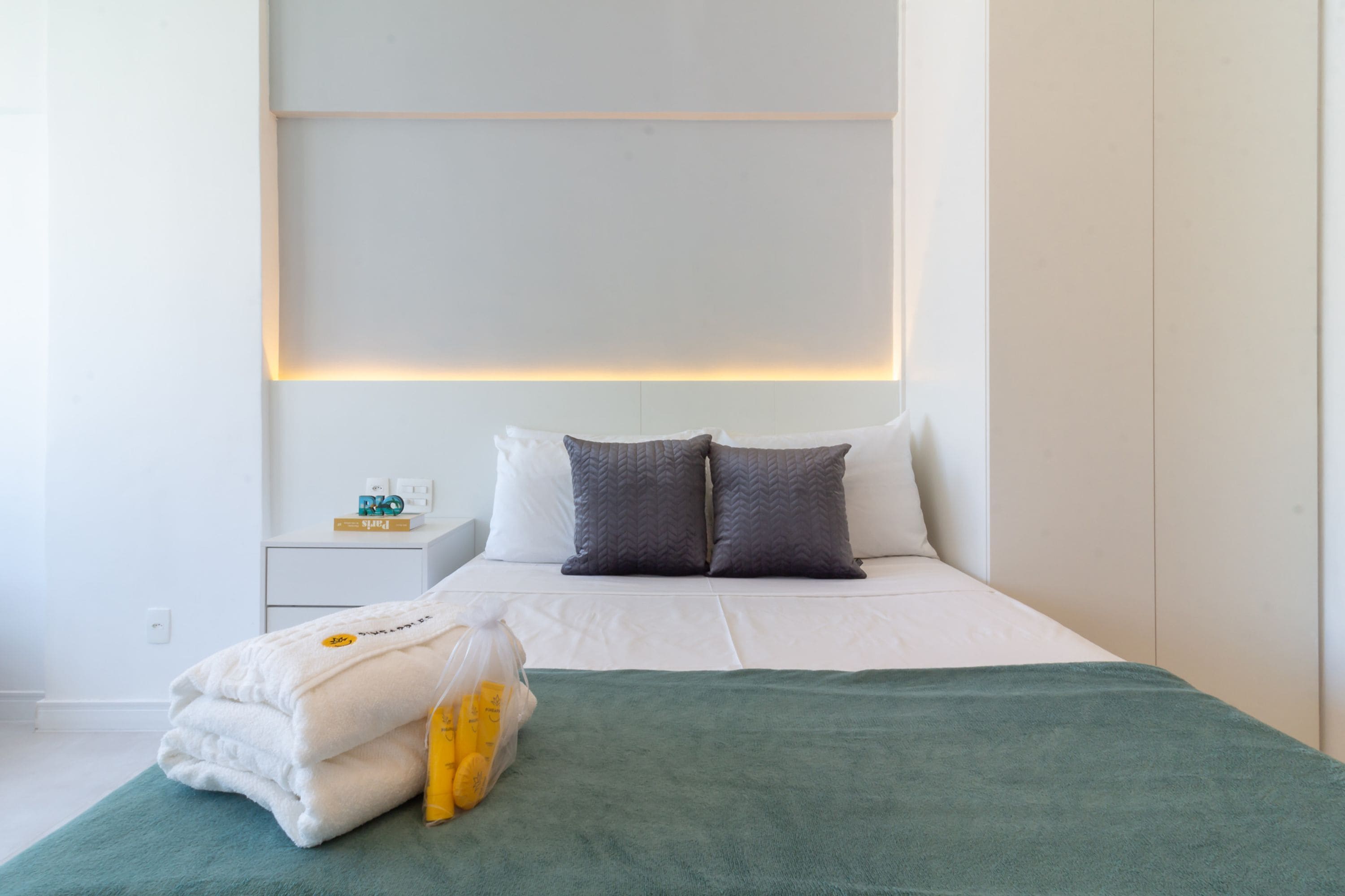 Et moderne hotelværelse med en pænt redt seng, et natbord med en lampe og en reol på væggen.