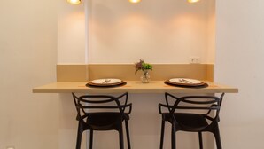 Un espace repas avec une table de couleur claire, deux chaises noires et trois lampes suspendues.
