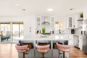 A modern kitchen with white cabinetry, a large island with bar stools, and a view of the outdoors. - Stylish Old Town Escape + Firepit*Heated Pool (Scottsdale)