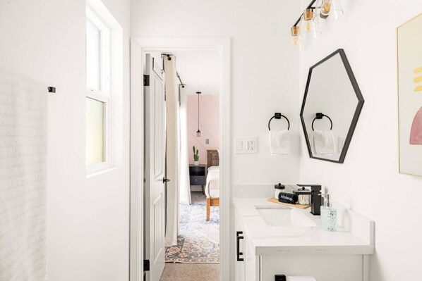 Un baño con lavamanos blanco, un espejo grande y cabina de ducha.