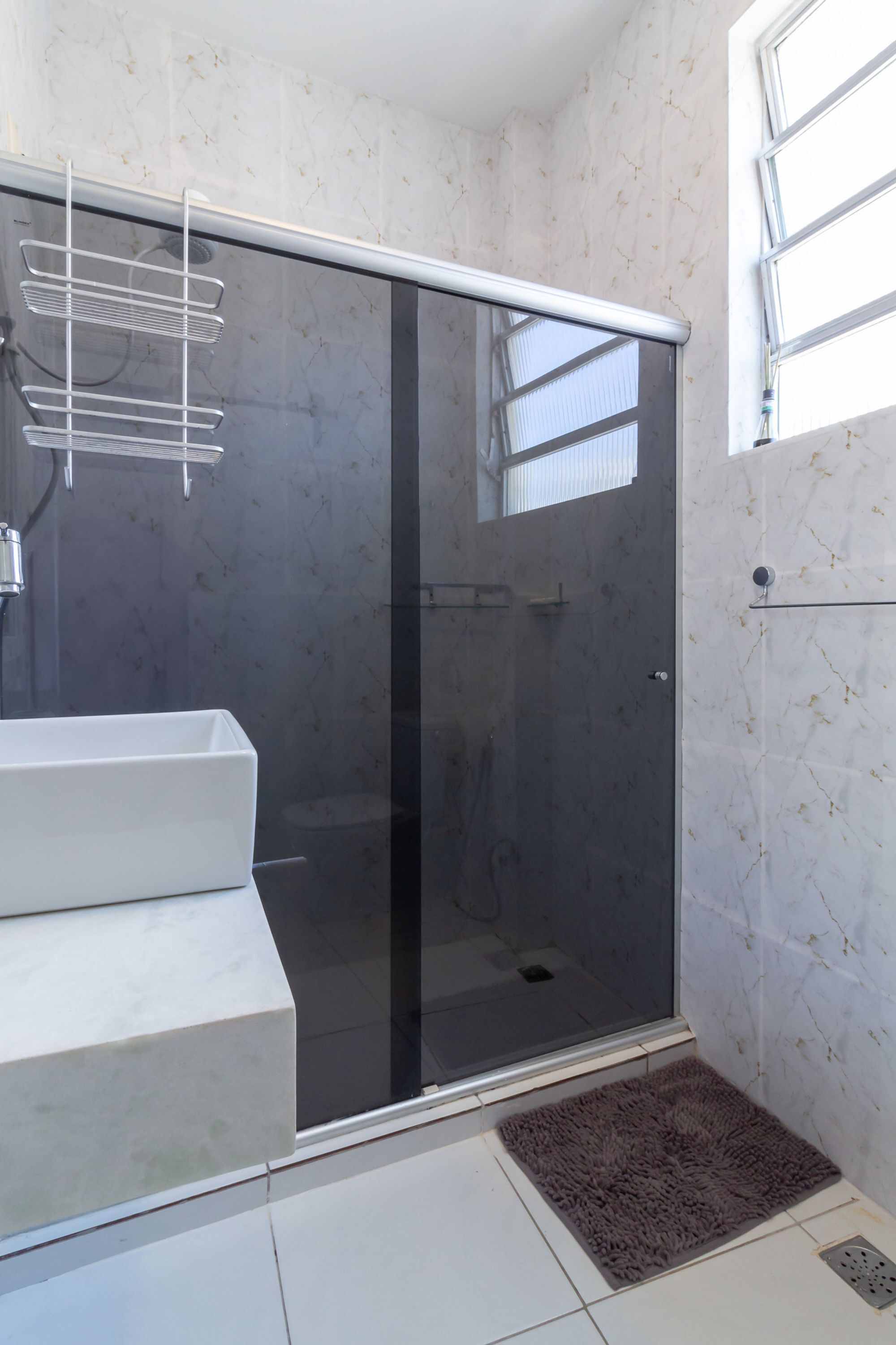 Ein modernes Badezimmer mit einer gläsernen Duschkabine, einem weißen Waschbecken und einer Marmor-Spritzschutzwand.