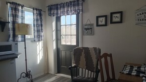 A cozy room with a wooden floor, a chair with a patterned throw, a table with a checkered tablecloth, and a wall with framed pictures of farm animals. - Charming bungalow in  historical Mancos with WiFi. Privacy and beautiful views. (Mancos)