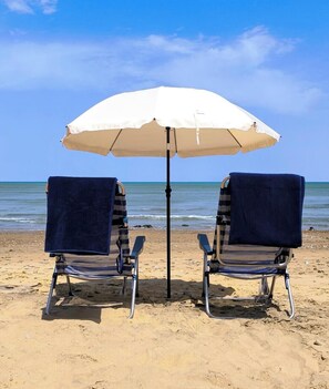 Two beach chairs with towels, a white umbrella, and a clear blue sky.