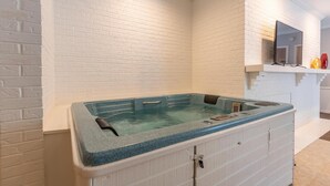 A spa room with a hot tub, white brick walls, and a flat-screen TV mounted above it. - Luxury Hot tub Suite w/ In-Room Hot Tub & King Bed 1BR, 1BA (Nashville)