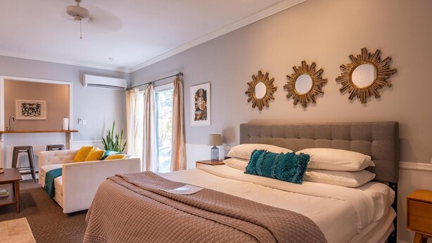 A bedroom with a large bed, a bedside table, a nightstand, a window with curtains, and wall-mounted decor. - Luxury Hot tub Suite w/ In-Room Hot Tub & King Bed 1BR, 1BA (Nashville)