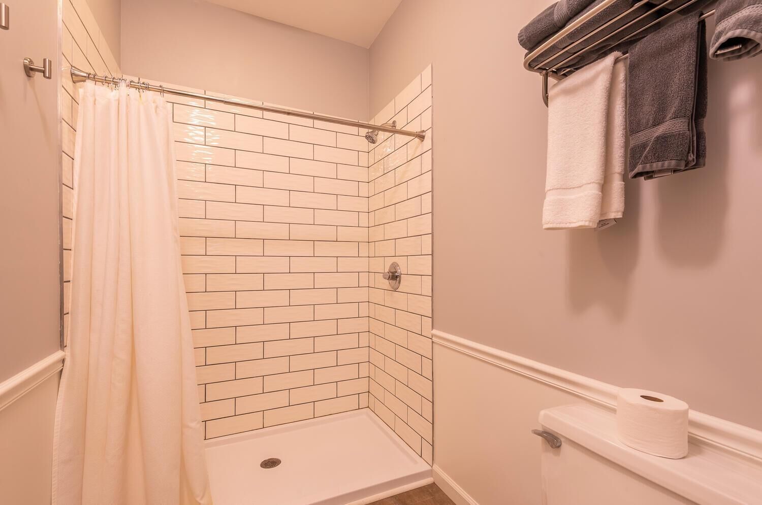 Een badkamer met een douche, witte betegelde wanden, een toilet en een handdoekrek met handdoeken.