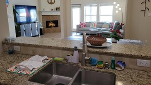A kitchen with a granite countertop, stainless steel sink, and a dining area with a gray sofa and a fireplace. - Island Waterfront 3/2 Private Pool & Hot Tub with Boat Dock (Corpus Christi)