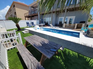A swimming pool with lounge chairs, a wooden bench, and a white fence.