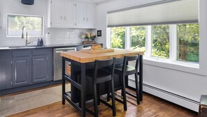 A modern kitchen with grey cabinets, a wooden island, black chairs, and a large window with a view of greenery. - Charming Home with Fireplace and Indoor Pool in Sharon, CT (Sharon)