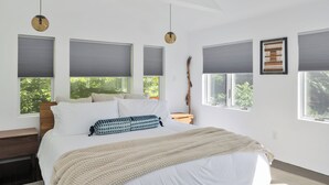 A modern bedroom with a large bed, grey blinds, a wooden nightstand, and a hanging light fixture. - Charming Home with Fireplace and Indoor Pool in Sharon, CT (Sharon)