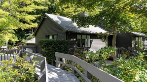 A house with a sloped roof, surrounded by dense greenery and a wooden deck. - Charming Home with Fireplace and Indoor Pool in Sharon, CT (Sharon)