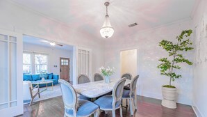 A dining area with a large table, chairs, and a chandelier. There is a potted plant on the right and a blue couch in the background. - Walkable SoCo Bungalow (Austin)