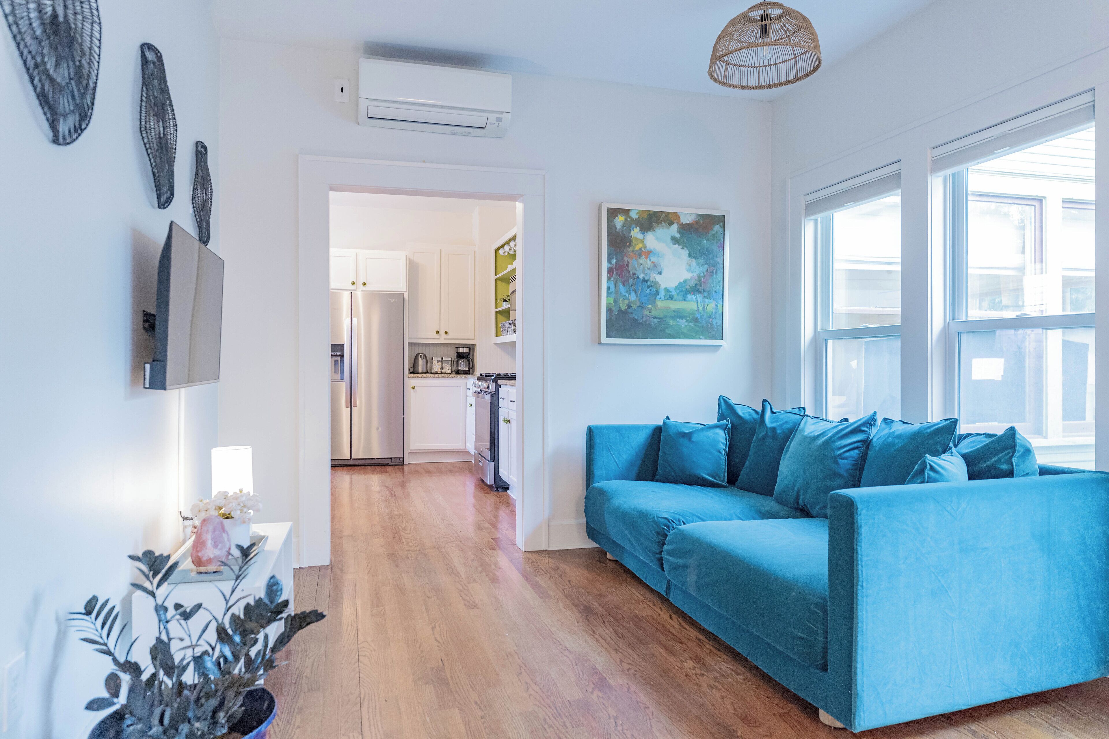 A modern living room with a blue sofa, wooden flooring, and a kitchen in the background.