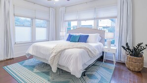 A bedroom with a large bed, white bedding, a ceiling fan, and a window with white curtains. - Walkable SoCo Bungalow (Austin)