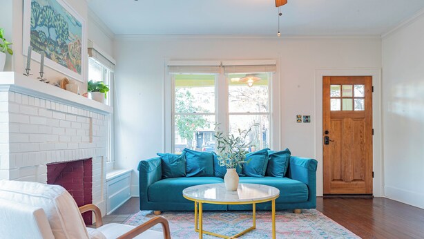 A living room with a blue sofa, a white armchair, a round coffee table, and a fireplace. - Walkable SoCo Bungalow (Austin)