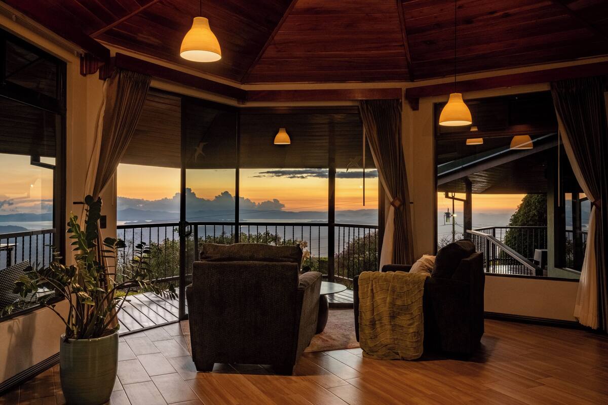 A room with a balcony, large windows, and a view of the sunset.