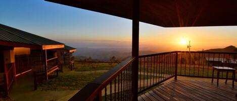A wooden deck with a metal railing overlooking a landscape with a sunset.