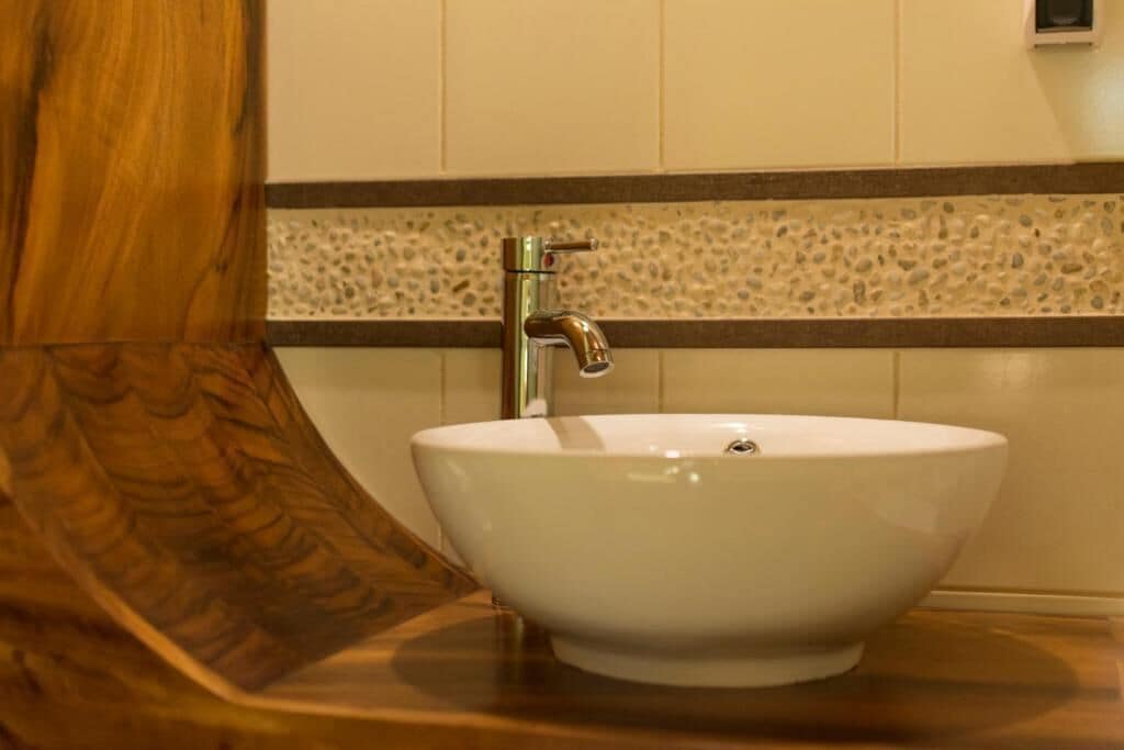 A white ceramic sink with a modern faucet, set against a wall with a textured tile border.