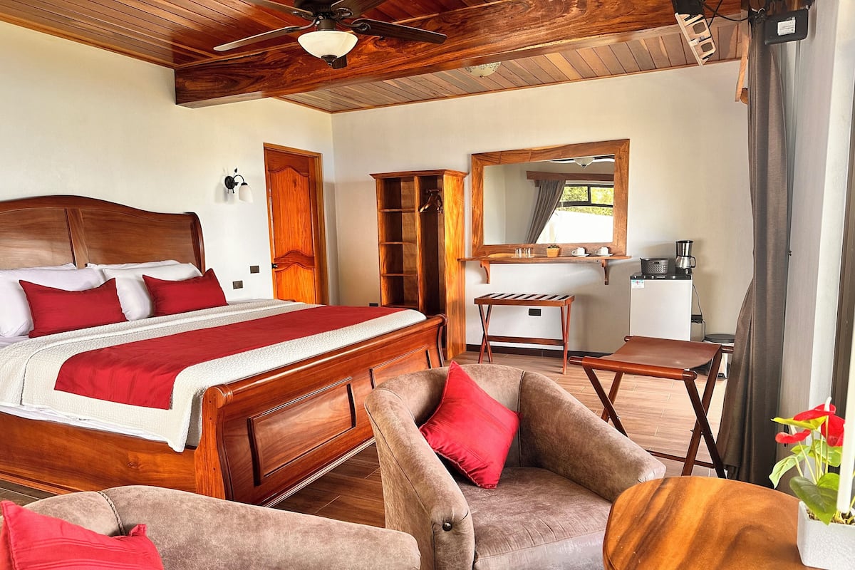 A bedroom with a wooden bed, red pillows, a wooden desk, and a chair.
