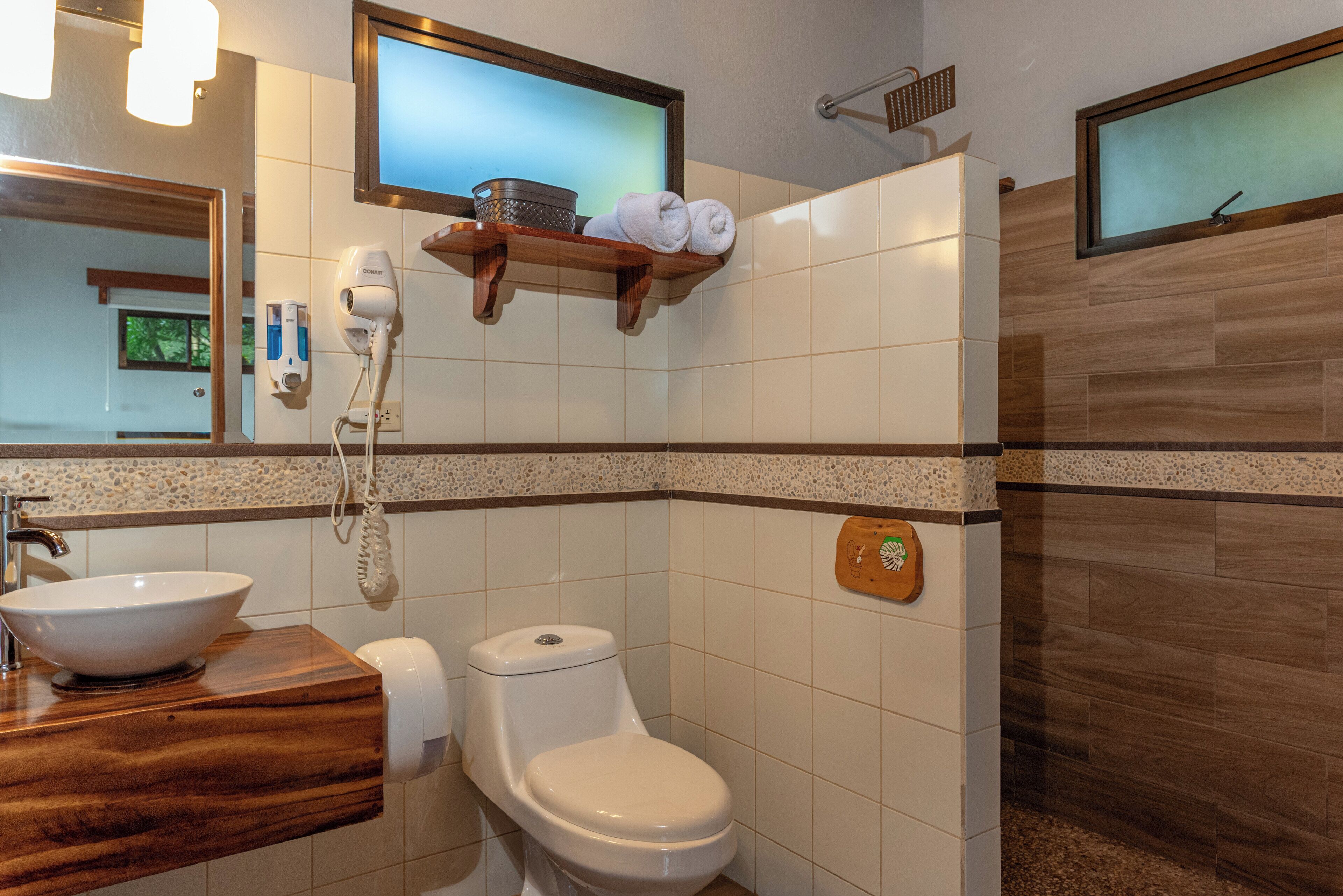 A bathroom with a wooden vanity, a white sink, a toilet, and a shower area.