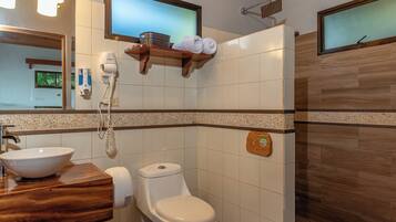 Un baño con tocador de madera, lavamanos blanco, inodoro y zona de ducha.