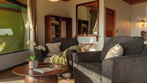 A cozy living room with a sofa, a coffee table with a magazine, a potted plant, and a large window with curtains. - Hotel Trópico Monteverde (Monteverde)