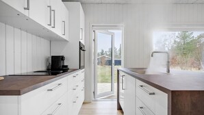 Cocina moderna con armarios blancos, encimera de madera, cafetera y vista al patio trasero a través de una puerta abierta.