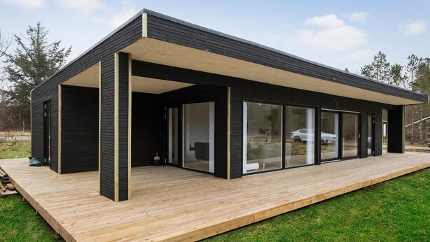 Una casa moderna con techo plano, amplios ventanales de vidrio y una terraza de madera.
