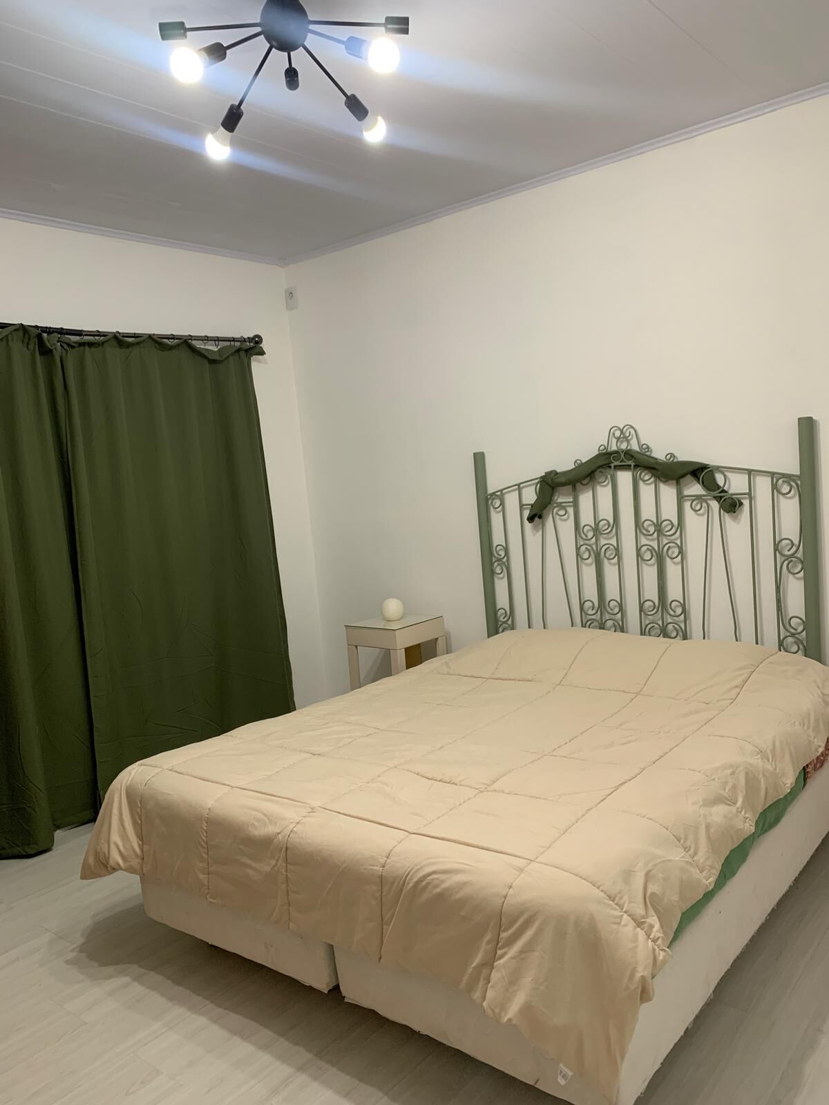 Um quarto com cama, ventilador de teto, mesa de cabeceira e cortinas verdes.