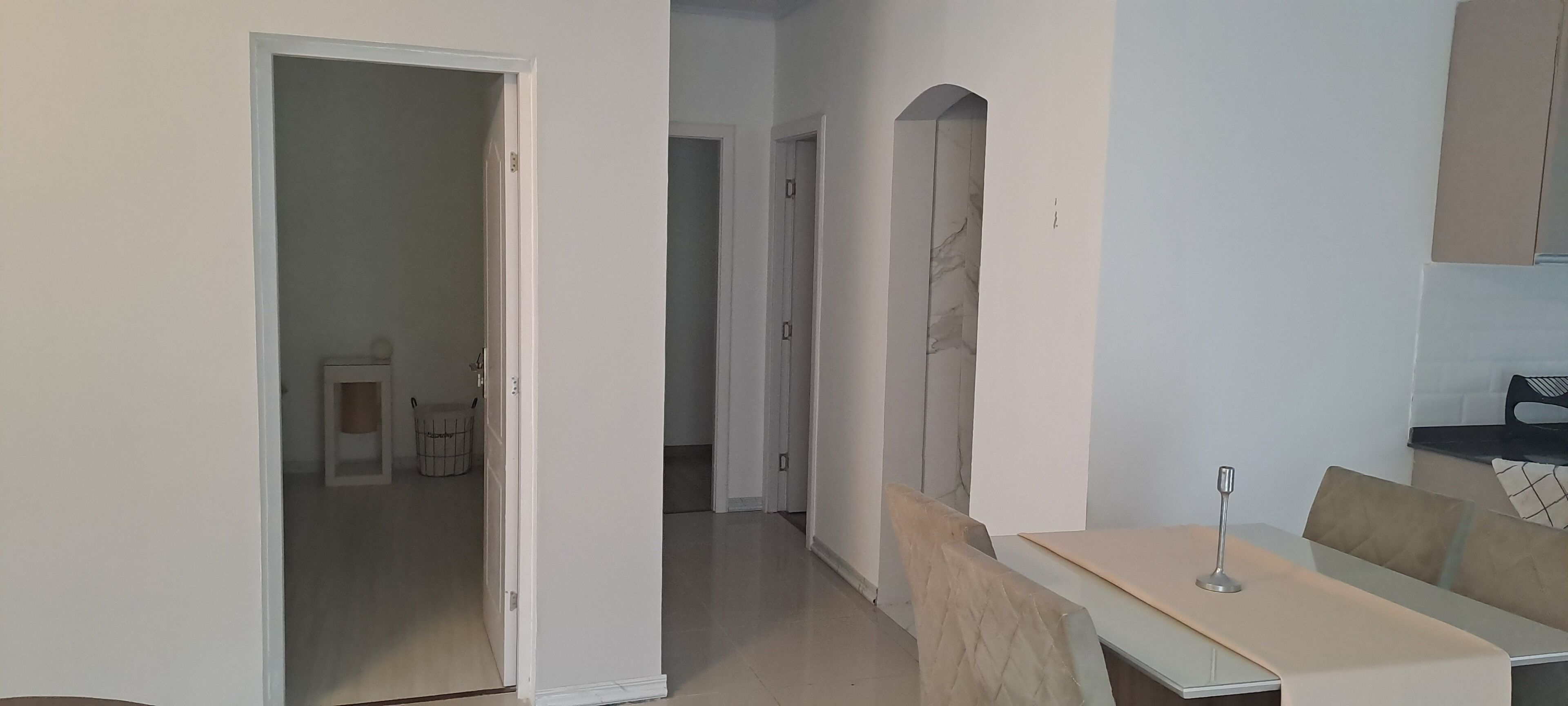 Una cucina moderna con mobili bianchi, una schiena a parete in marmo e una zona pranzo con tavolo e sedie.
