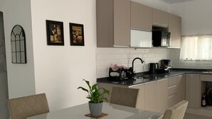 Una cocina moderna con comedor. Incluye una mesa blanca con cuatro sillas, un microondas, un lavamanos y una planta en maceta.