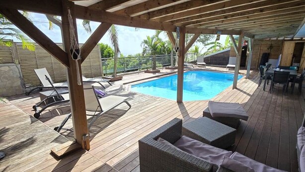 Un espace piscine extérieur abrité, doté d’une terrasse en bois, de chaises longues et d’une structure en forme de pergola.