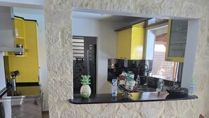 Une cuisine avec un mur en pierre, un plan de travail noir et deux chaises.