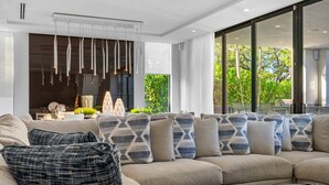 Uma sala de estar moderna com um sofá grande, almofadas estampadas, uma mesa de centro e uma área de jantar com mesa e cadeiras.