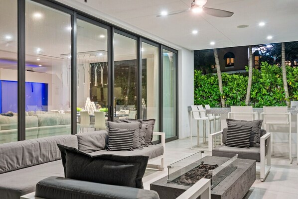 Un espacio exterior moderno con sala, sillas y una chimenea.