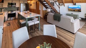 Un loft espacioso con techo alto, vigas de madera, cocina equipada con electrodomésticos modernos, comedor con mesa redonda y un espacio de sala de estar acogedor con sofá y televisor.