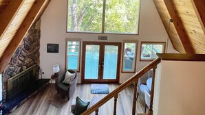 Un dormitorio acogedor en un ático con un ventanal grande, vigas de madera, una pared de piedra y una escalera.