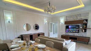 A modern dining area with a wooden table set for six, a sofa, and a television mounted on the wall. - Urban Sanctuary in the Heart of Dushanbe w/Stunning Views Steps from Rudaki Park (Dushanbe)