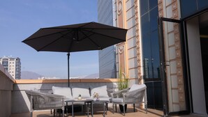 A rooftop terrace with outdoor furniture, a large umbrella, and a view of a modern building. - Urban Sanctuary in the Heart of Dushanbe w/Stunning Views Steps from Rudaki Park (Dushanbe)
