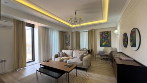 A modern living room with a sofa, coffee table, and a dining area with a laptop and books. - Urban Sanctuary in the Heart of Dushanbe w/Stunning Views Steps from Rudaki Park (Dushanbe)