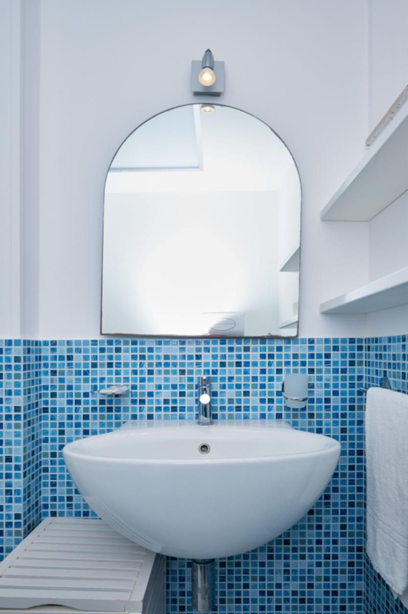 A bathroom with a white sink, blue mosaic tiles, a mirror, and a towel rack.